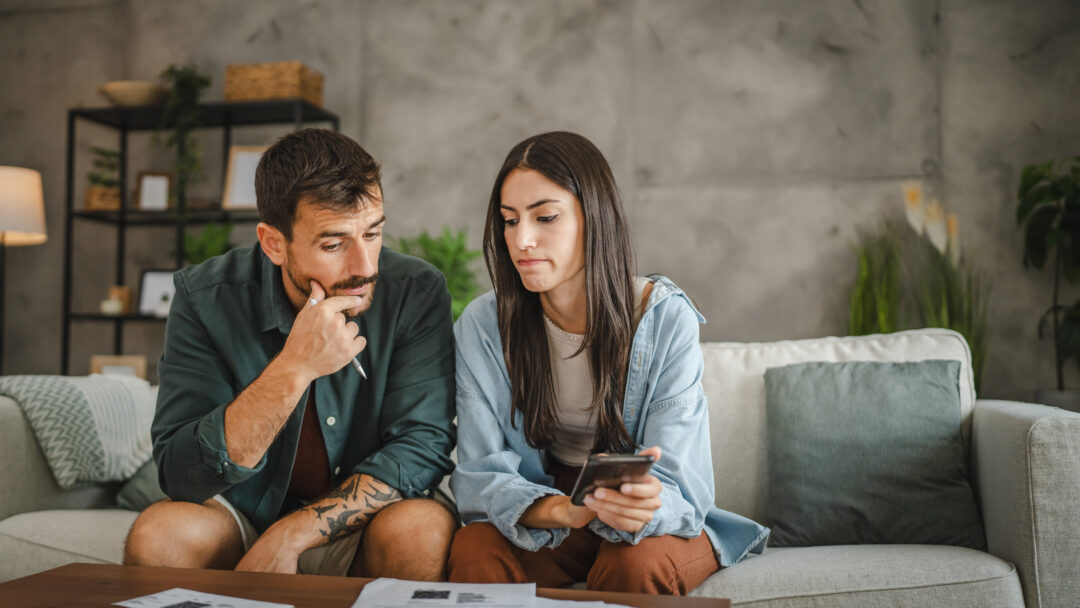 Two adults looking at financial documents together at home, checking information on a smartphone.