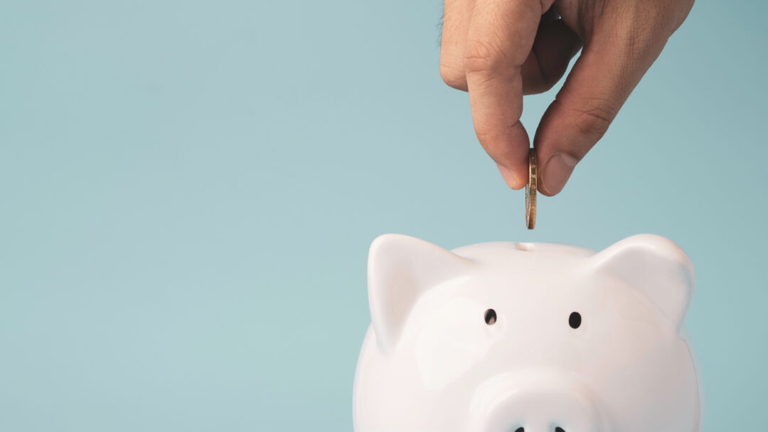 Hand putting coin to white piggy bank saving on blue background