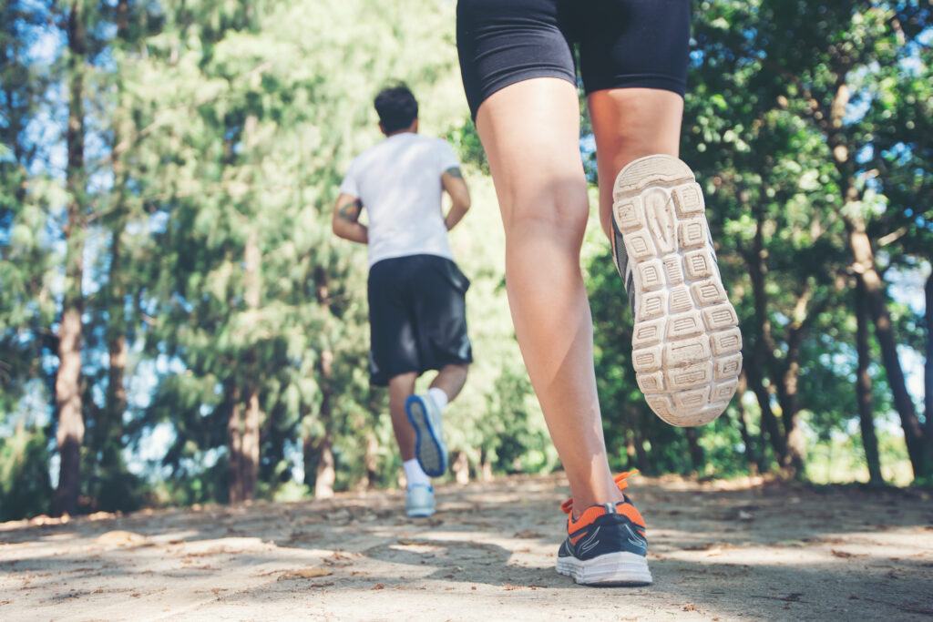 Close-up of two people running on a dirt trail, with focus on legs and shoes in motion