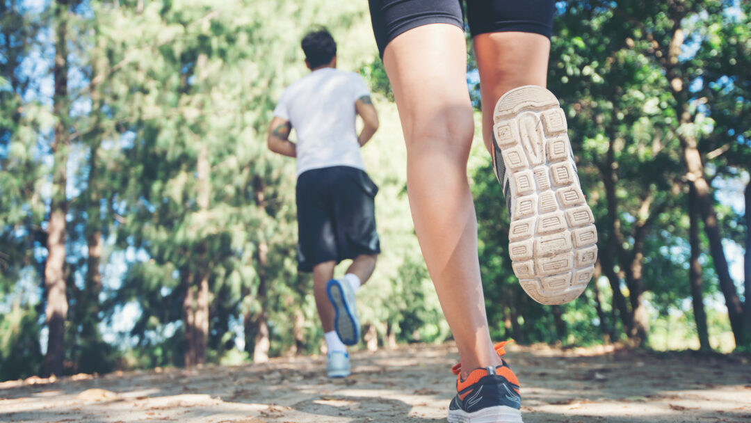 Close-up of two people running on a dirt trail, with focus on legs and shoes in motion