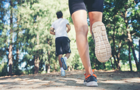 Close-up of two people running on a dirt trail, with focus on legs and shoes in motion