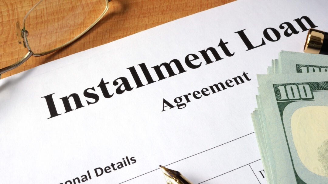 Close-up of an installment loan agreement document with cash, a pen, and eyeglasses on a desk