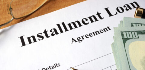 Close-up of an installment loan agreement document with cash, a pen, and eyeglasses on a desk
