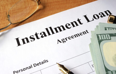 Close-up of an installment loan agreement document with cash, a pen, and eyeglasses on a desk