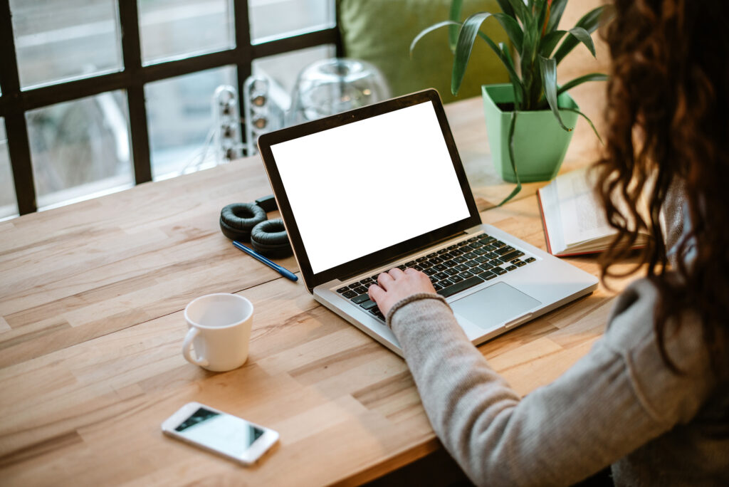 Person working on a laptop at a desk, with a coffee cup, phone, and headphones nearby