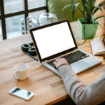 Person working on a laptop at a desk, with a coffee cup, phone, and headphones nearby