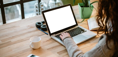 Person working on a laptop at a desk, with a coffee cup, phone, and headphones nearby
