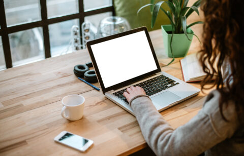 Person working on a laptop at a desk, with a coffee cup, phone, and headphones nearby