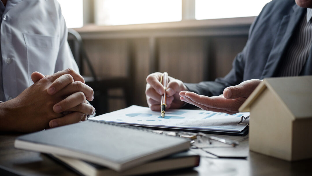 Two people reviewing financial documents at a desk, with one person pointing to a chart on a report.