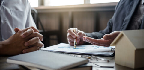 Two people reviewing financial documents at a desk, with one person pointing to a chart on a report.