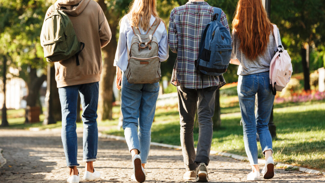 Group of college-age students walking across campus with backpacks between classes.