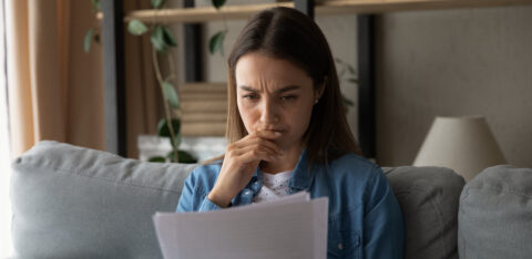 Person sitting on a couch reading a document with a concerned expression, hand near their mouth