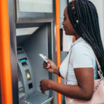 APerson using an ATM, holding a card while standing in front of the machine
