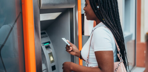 APerson using an ATM, holding a card while standing in front of the machine