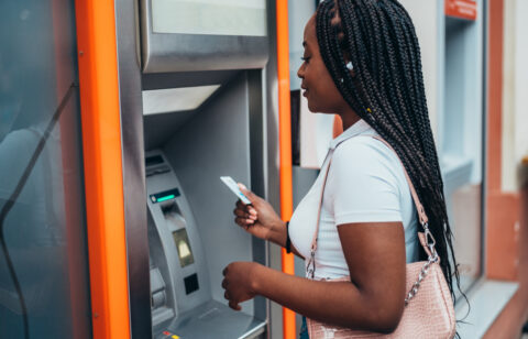 APerson using an ATM, holding a card while standing in front of the machine