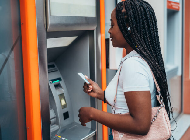 APerson using an ATM, holding a card while standing in front of the machine
