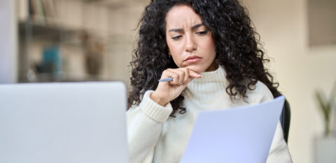 Person reviewing a document with a concerned expression while sitting at a desk with a laptop