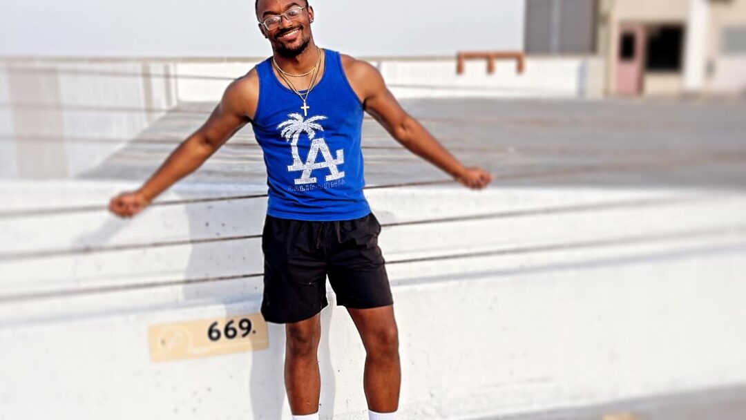 Man standing on a rooftop parking area, smiling and leaning back against a concrete barrier