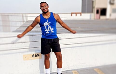 Man standing on a rooftop parking area, smiling and leaning back against a concrete barrier