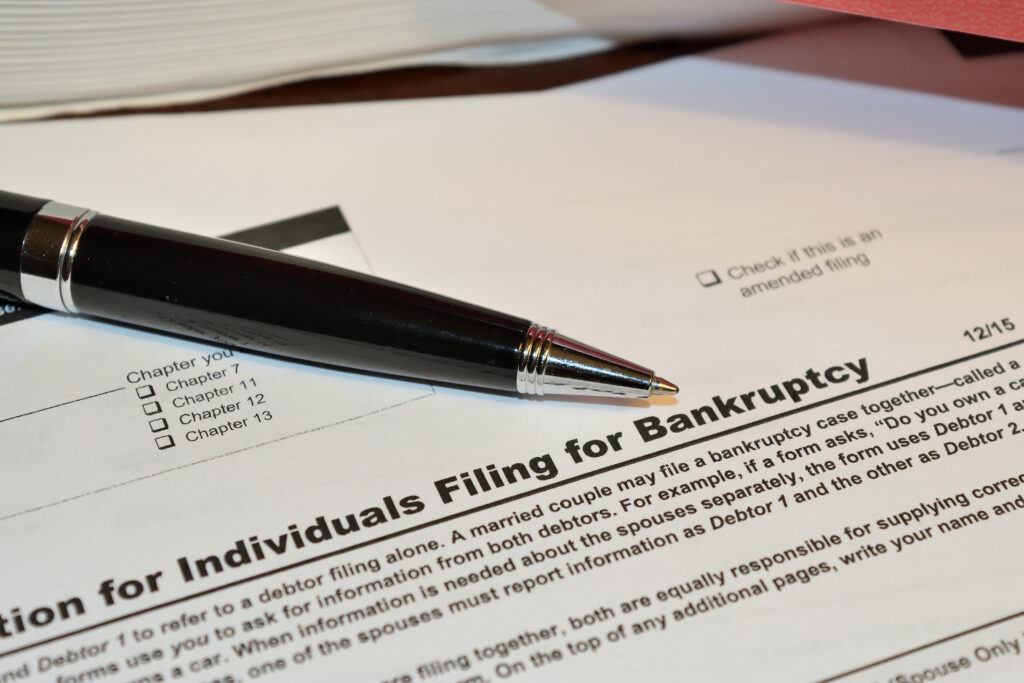 Close-up of a bankruptcy filing form with a pen resting on the document, showing filing chapter options and amended filing checkbox.