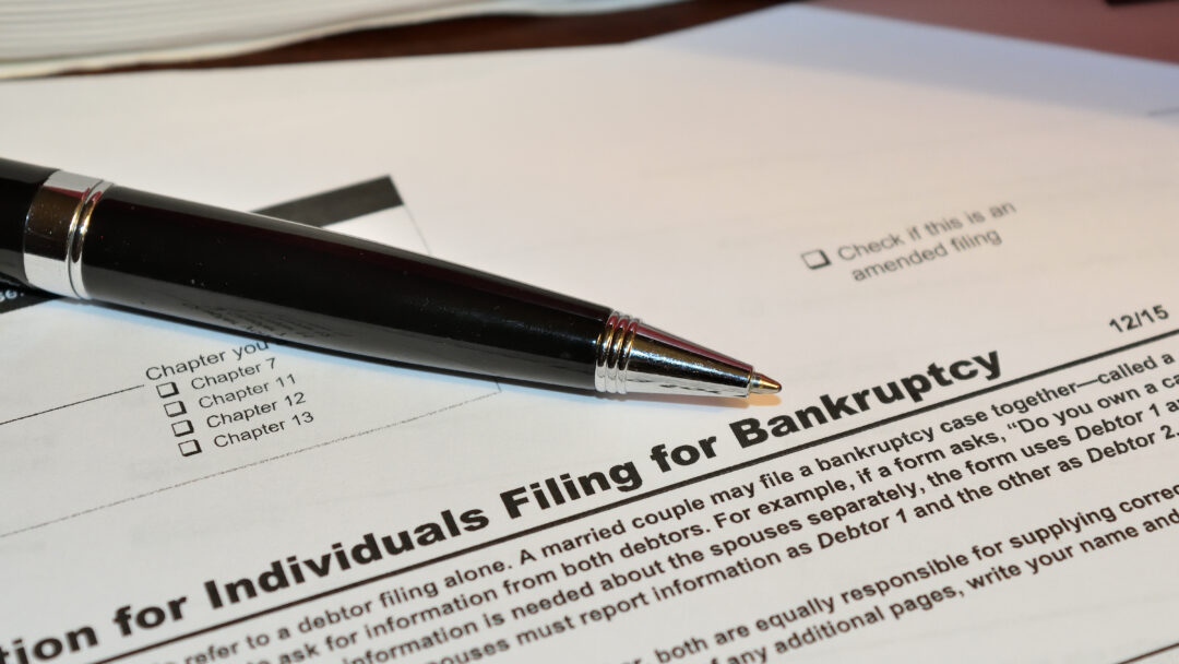 Close-up of a bankruptcy filing form with a pen resting on the document, showing filing chapter options and amended filing checkbox.