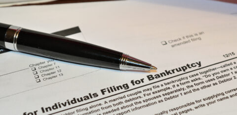 Close-up of a bankruptcy filing form with a pen resting on the document, showing filing chapter options and amended filing checkbox.