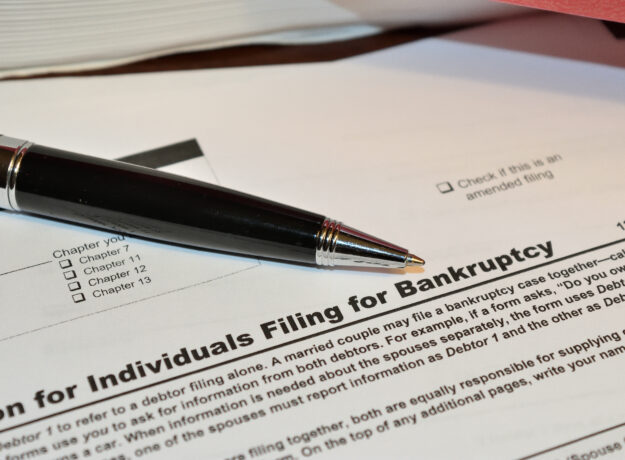 Close-up of a bankruptcy filing form with a pen resting on the document, showing filing chapter options and amended filing checkbox.