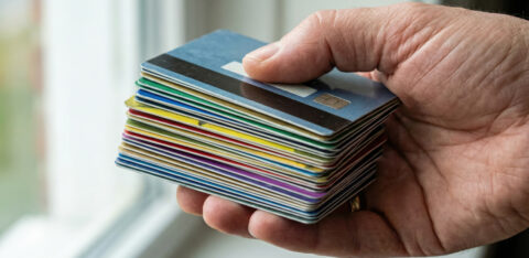 Close-up of a hand holding a stack of colorful credit cards near a window.