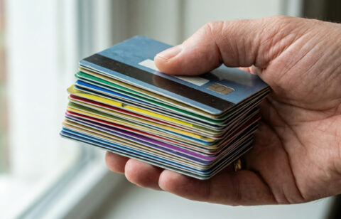 Close-up of a hand holding a stack of colorful credit cards near a window.