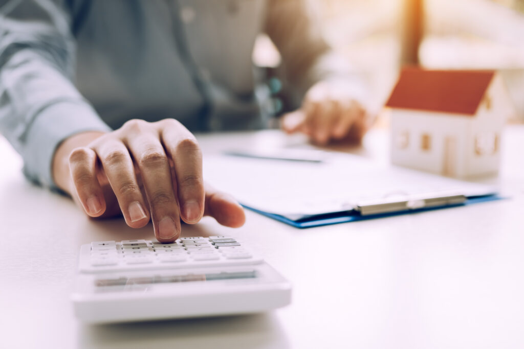 Person using a calculator beside a miniature house model and mortgage paperwork.