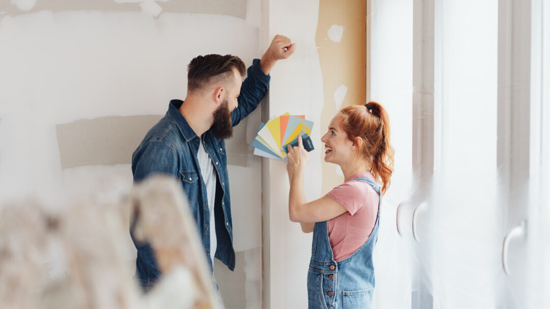 Couple choosing paint color samples while renovating a room in their home, smiling as they plan a home improvement project.