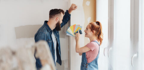 Couple choosing paint color samples while renovating a room in their home, smiling as they plan a home improvement project.