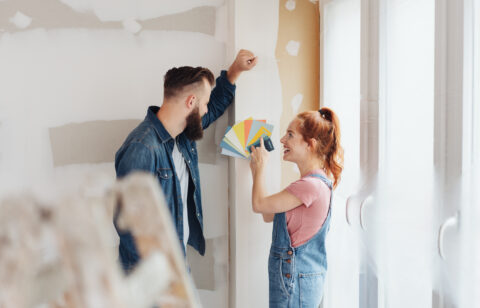 Couple choosing paint color samples while renovating a room in their home, smiling as they plan a home improvement project.