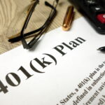 Close-up of a 401(k) retirement plan document with a calculator, eyeglasses, and pens on a desk.
