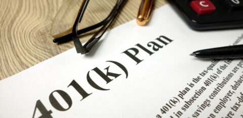 Close-up of a 401(k) retirement plan document with a calculator, eyeglasses, and pens on a desk.