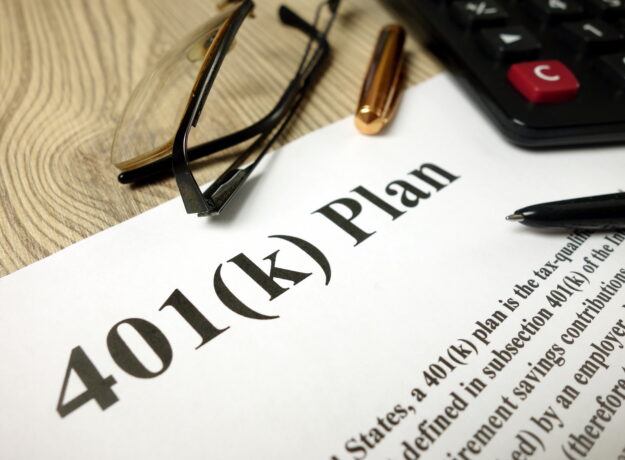 Close-up of a 401(k) retirement plan document with a calculator, eyeglasses, and pens on a desk.