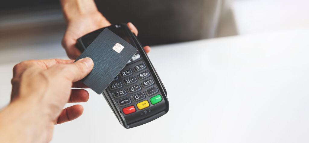 Person tapping a credit card on a payment terminal to complete a contactless purchase.