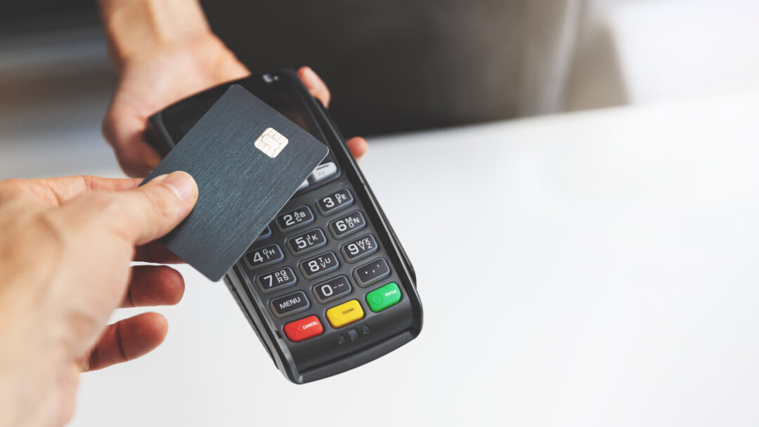 Person tapping a credit card on a payment terminal to complete a contactless purchase.
