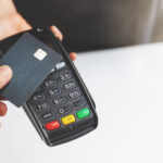 Person tapping a credit card on a payment terminal to complete a contactless purchase.