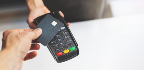 Person tapping a credit card on a payment terminal to complete a contactless purchase.