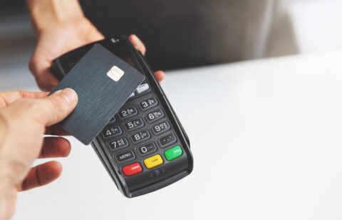 Person tapping a credit card on a payment terminal to complete a contactless purchase.