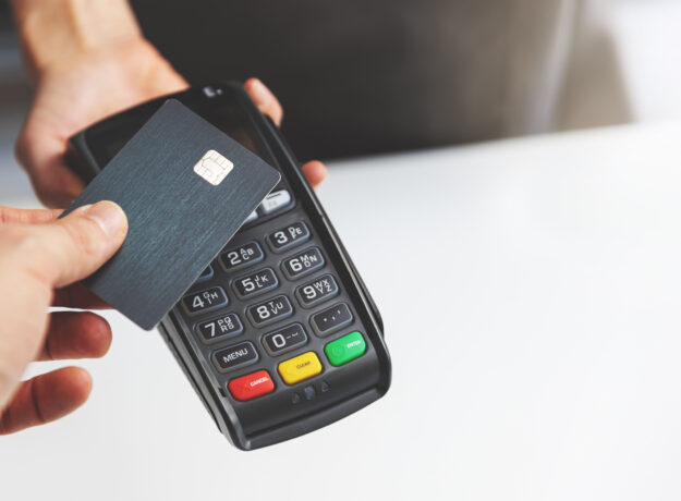 Person tapping a credit card on a payment terminal to complete a contactless purchase.