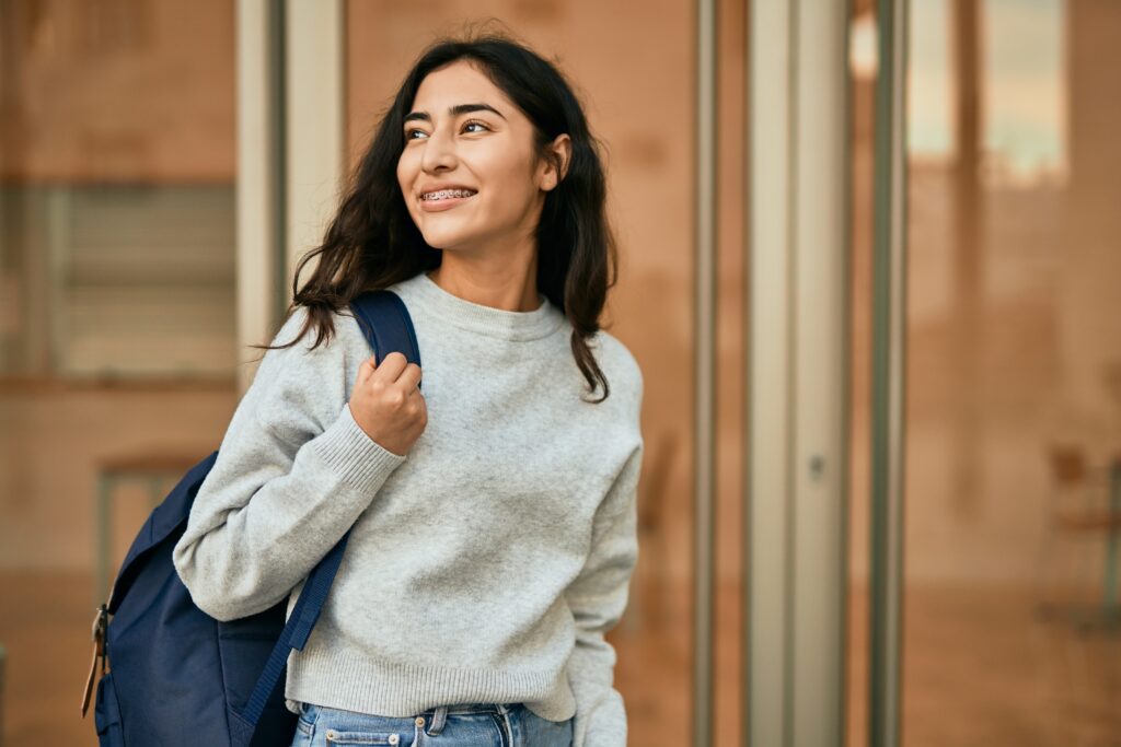 Smiling female college student wearing a backpack outside an academic building, representing higher education and campus life.