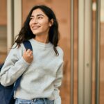 Smiling female college student wearing a backpack outside an academic building, representing higher education and campus life.
