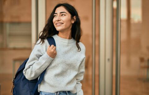Smiling female college student wearing a backpack outside an academic building, representing higher education and campus life.