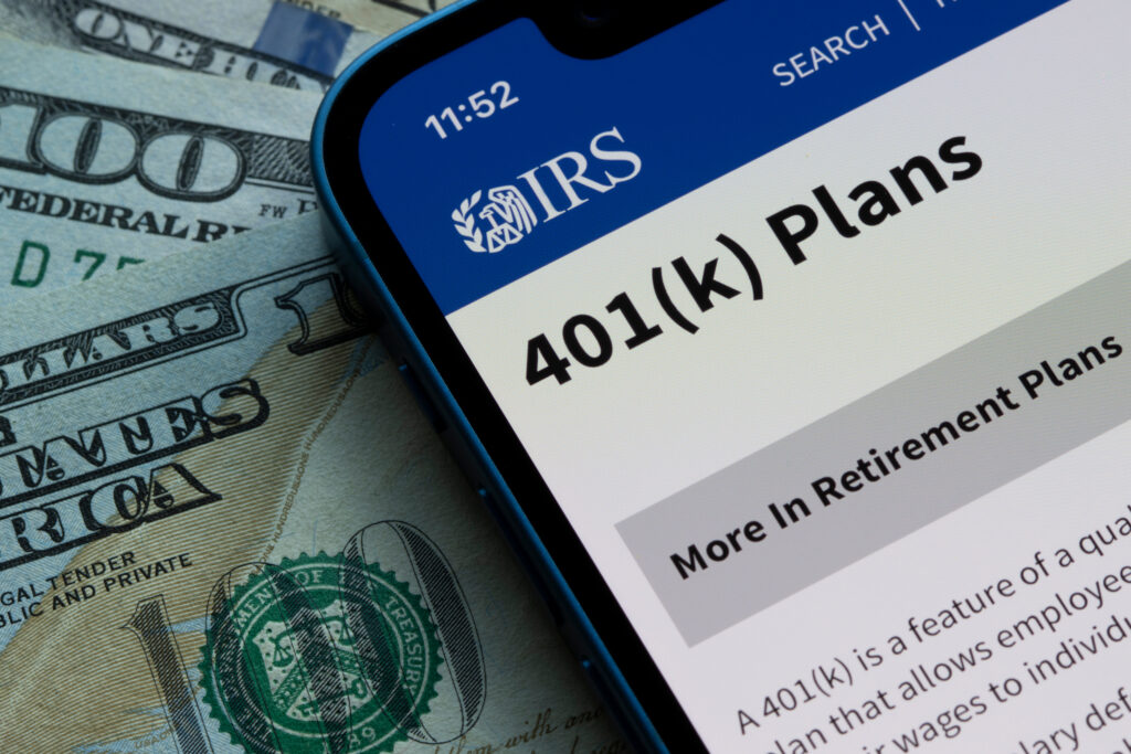 Smartphone displaying the IRS 401(k) Plans webpage on top of U.S. dollar bills.