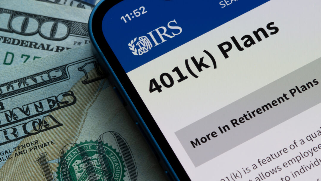 Smartphone displaying the IRS 401(k) Plans webpage on top of U.S. dollar bills.