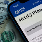 Smartphone displaying the IRS 401(k) Plans webpage on top of U.S. dollar bills.