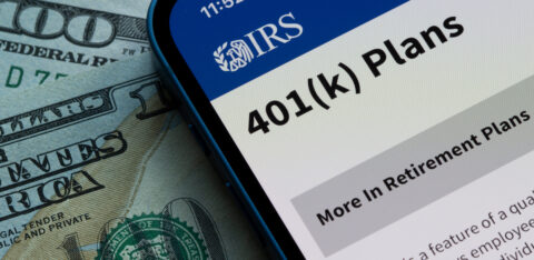 Smartphone displaying the IRS 401(k) Plans webpage on top of U.S. dollar bills.
