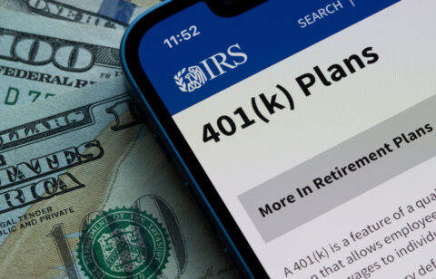 Smartphone displaying the IRS 401(k) Plans webpage on top of U.S. dollar bills.